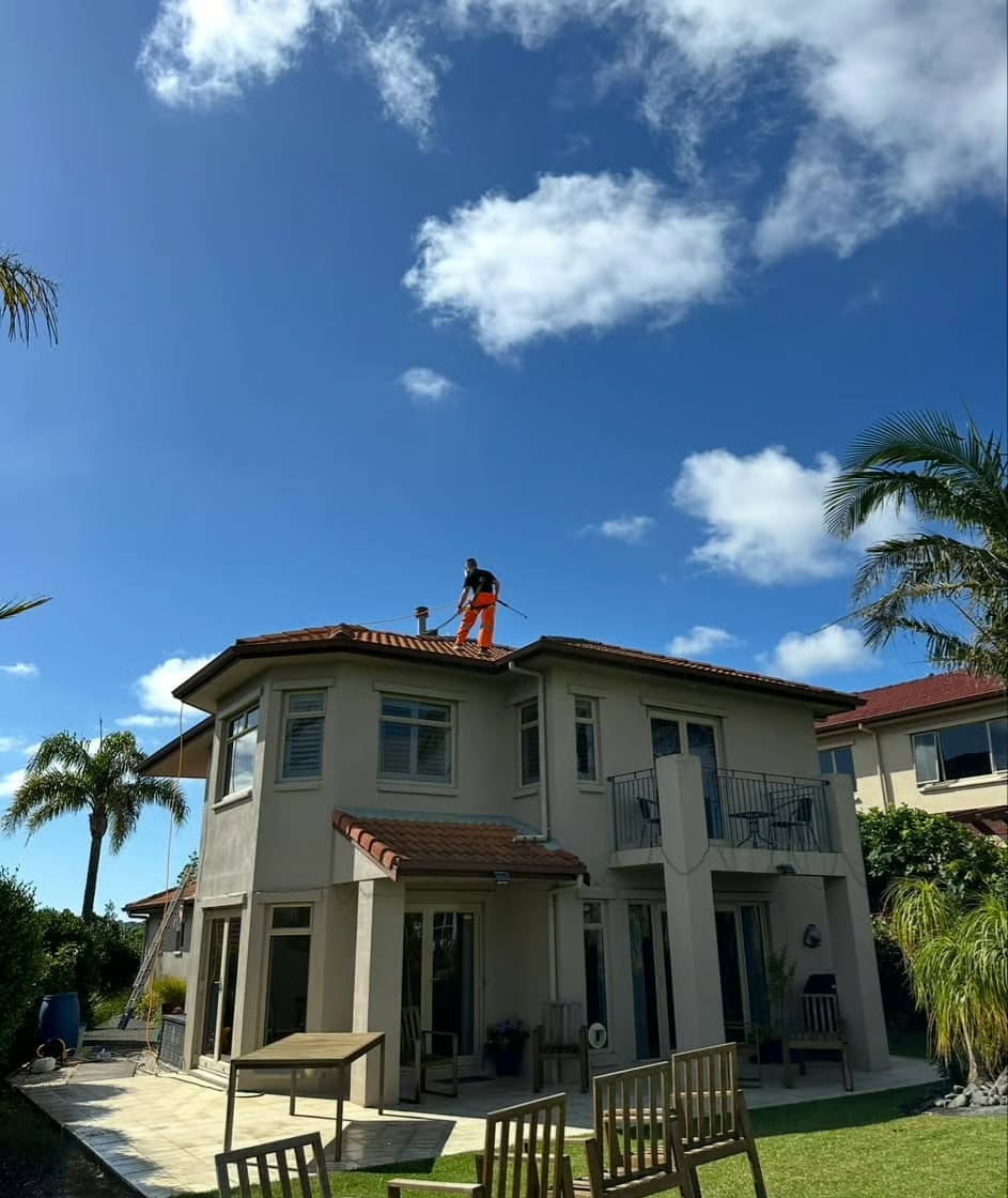 Professional roof cleaning service in Auckland with worker using pressure washing equipment on red tile roof